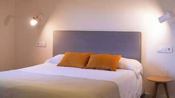 A bedroom with a bed, wooden beams, a bedside table, and wall-mounted lights.
