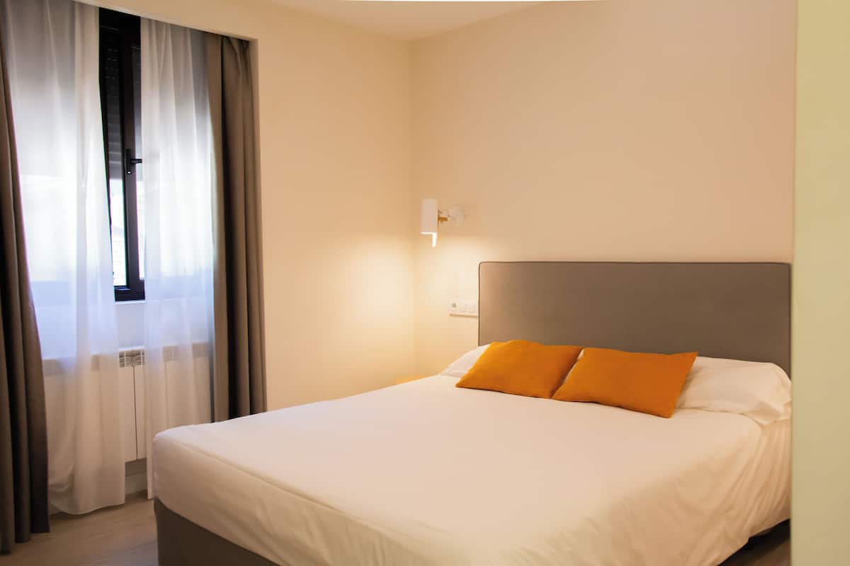 Ein Hotelzimmer mit Bett, Vorhängen, einer Wandleuchte und einem Fenster mit Blick.