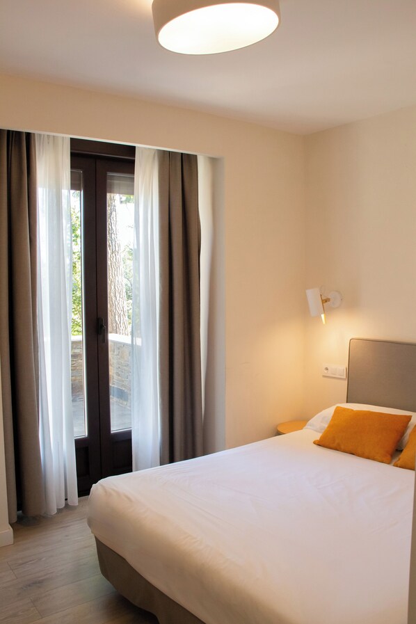 A hotel room with a bed, a nightstand, a wall-mounted lamp, and a view through a door with curtains. - Hotel Villalucerna (Vigo)