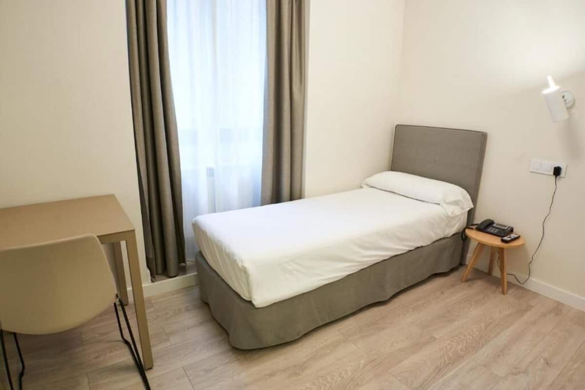 Ein kleiner, ordentlicher Raum mit einem Bett, einem Schreibtisch und einem Stuhl.