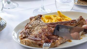 A plate with a steak and fries, a fork, and a knife on a table with a white tablecloth.
