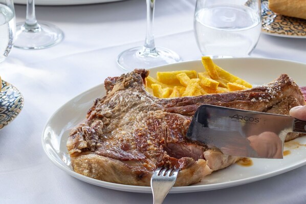 A plate with a steak and fries, a fork, and a knife on a table with a white tablecloth. - Hotel Villalucerna (Vigo)