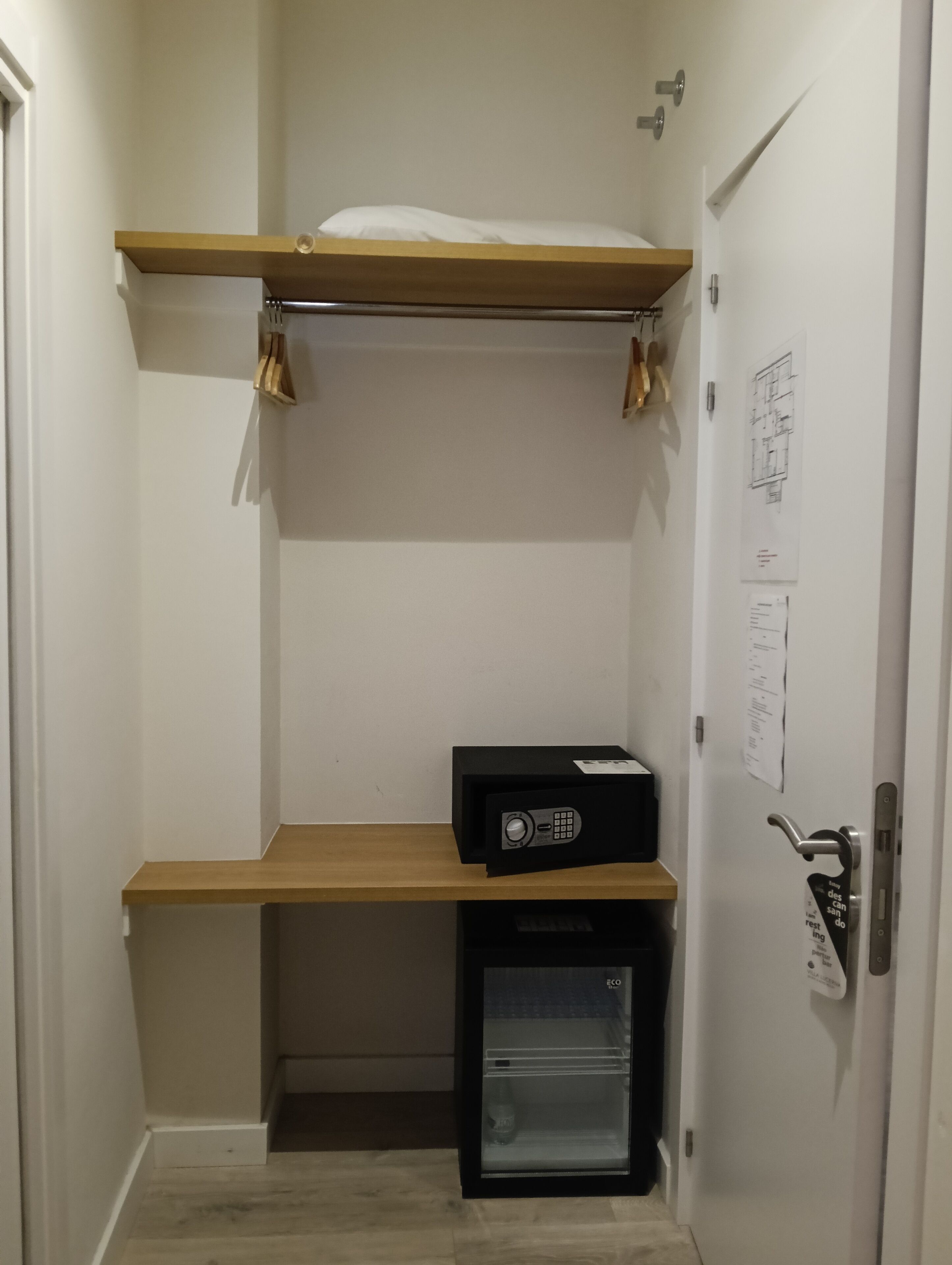 Un módulo de almacenamiento compacto con un pequeño refrigerador, un estante de madera y una puerta blanca con cerradura y cerradura para llave.