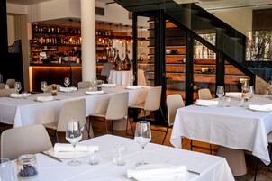 Un restaurante con varias mesas dispuestas para comer, una zona de bar con estantes llenos de botellas y una escalera que lleva a un área exterior.