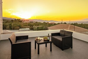A terrace with wicker furniture, a table with a bottle and glasses, and a view of the sunset over the sea. - Seaview Villa Volter  (Zakynthos)