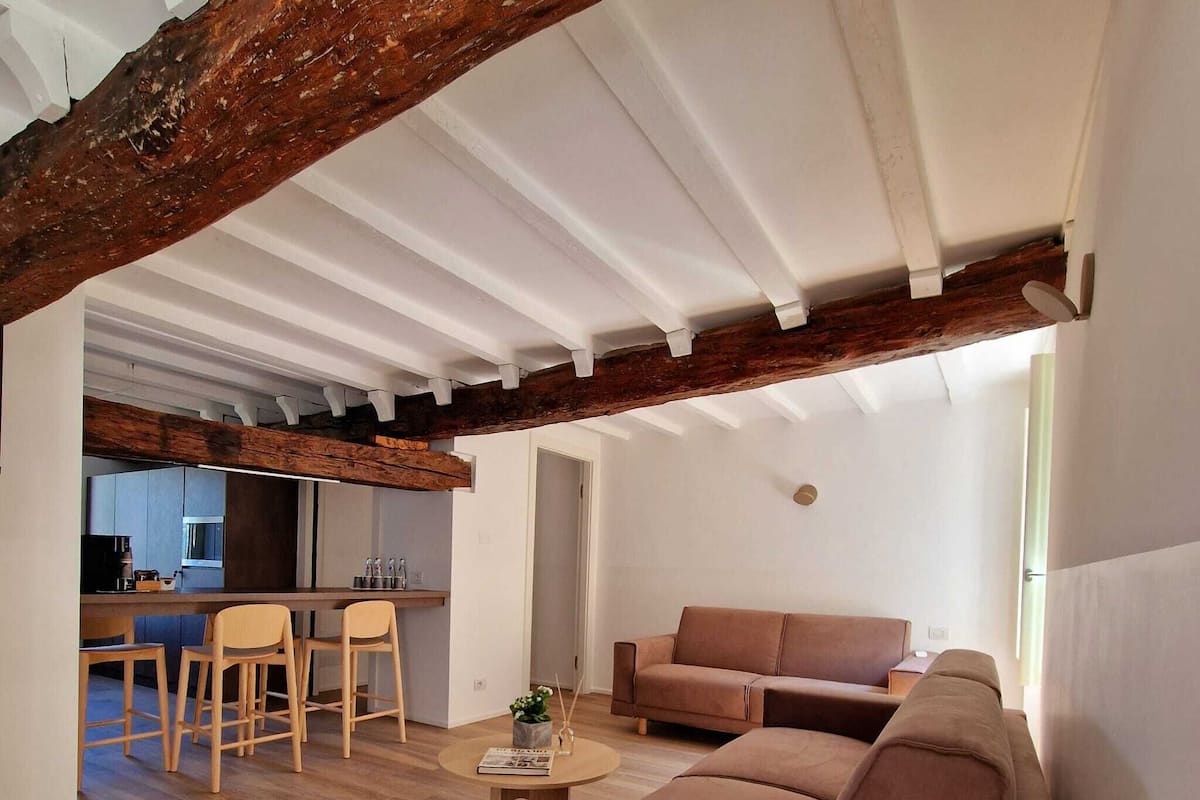 Un salon moderne avec un canapé, une table basse et un coin repas comprenant des chaises, et une cuisine en arrière-plan.