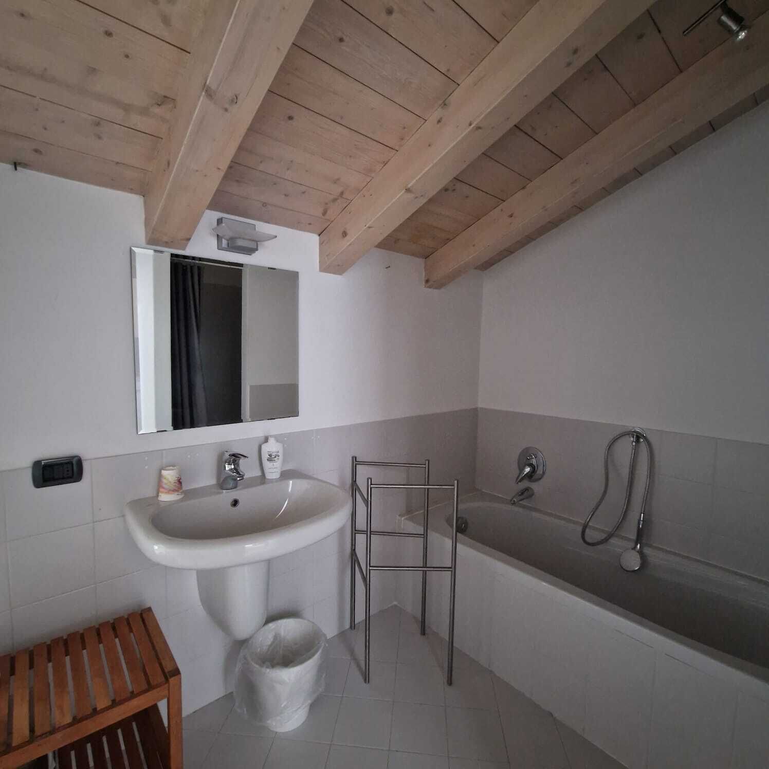 Een badkamer met een houten plafond, een wastafel, een spiegel, een bad en een houten bankje.