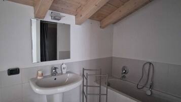 Een badkamer met een houten plafond, een wastafel, een spiegel, een bad en een houten bankje.
