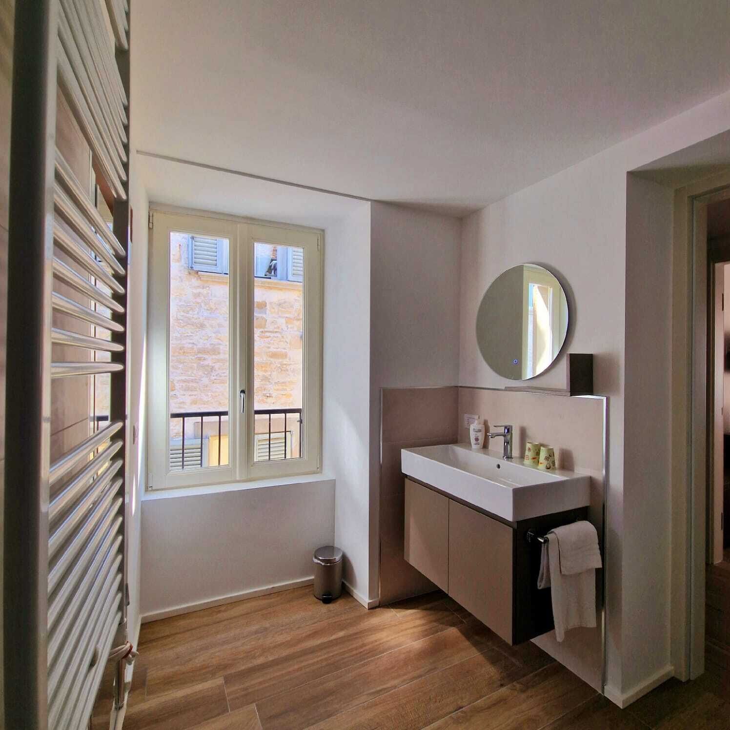 A modern bathroom with a window, a sink, a mirror, and a trash bin.