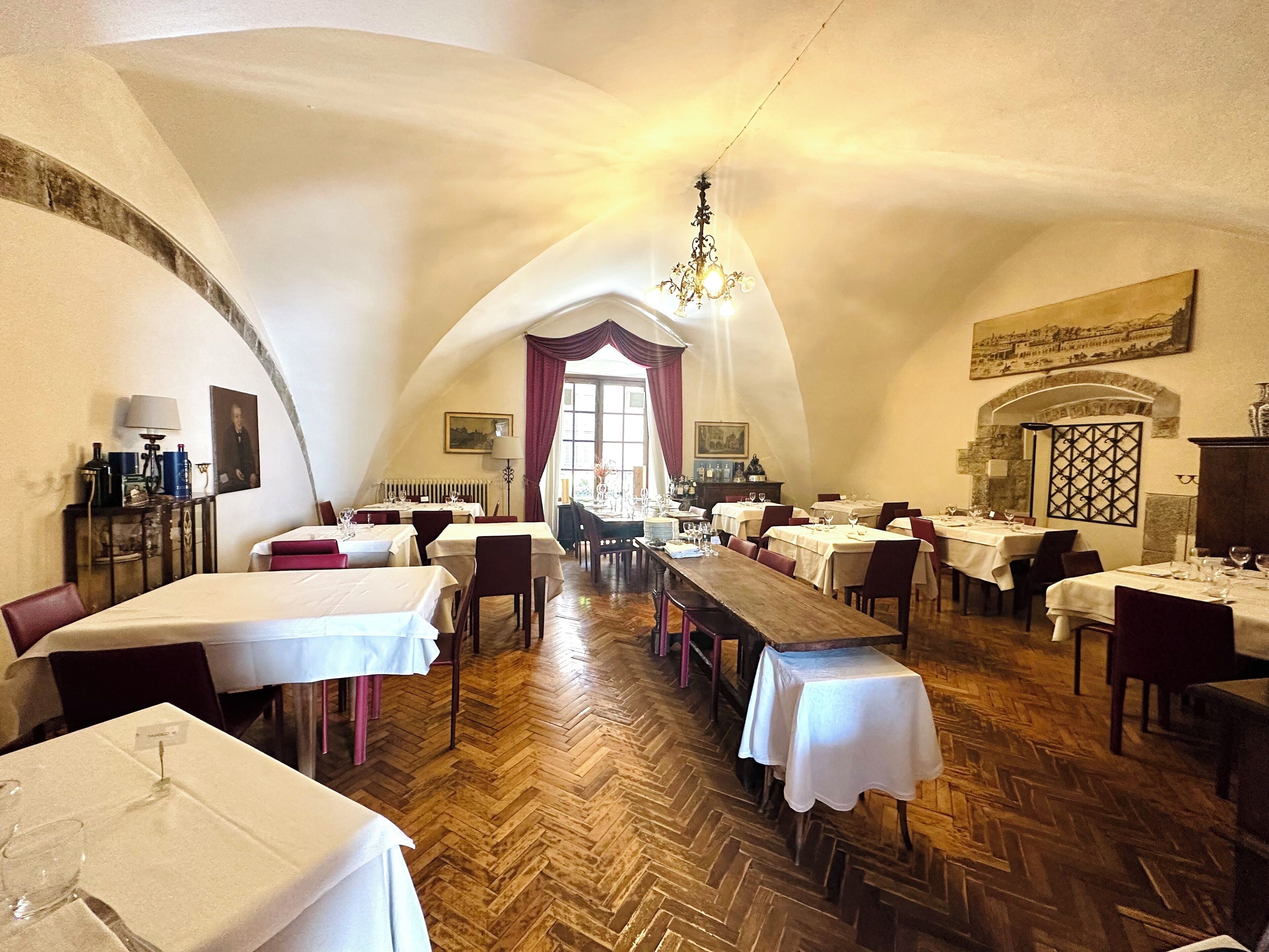 Restaurante com altos tetos abobadados, soalho de madeira em padrão herringbone e mesas preparadas para refeições.