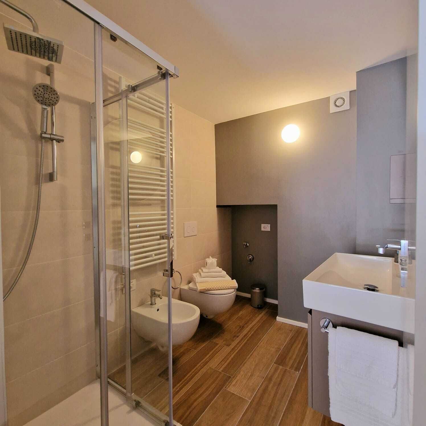 A modern bathroom with a glass shower enclosure, a bidet, a sink, and a toilet.