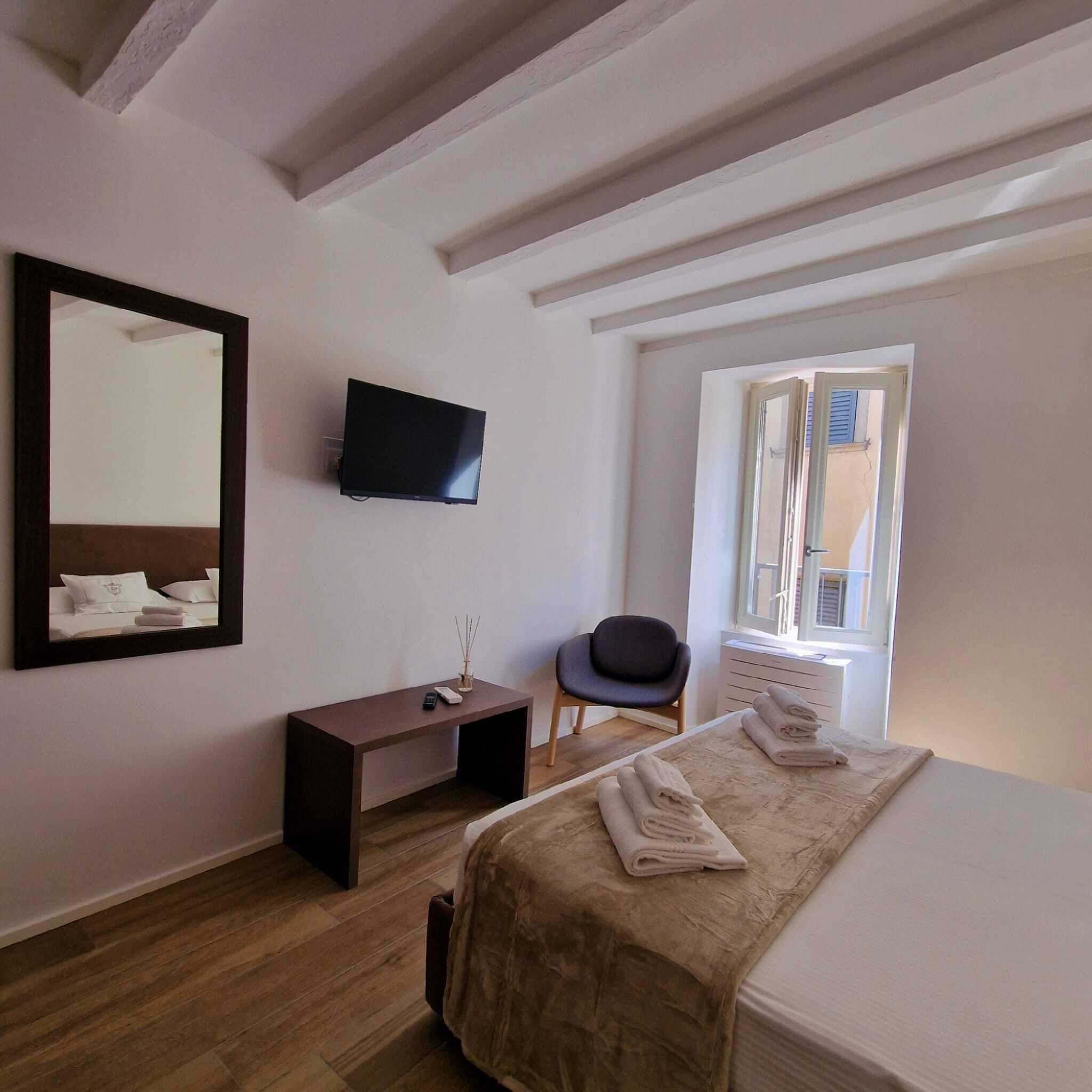A hotel room with a bed, a TV mounted on the wall, a desk, a chair, and a window with blinds.