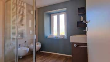 Uma casa de banho moderna com cabine de duche em vidro, sanita encastrada e janela que permite a entrada de luz natural.