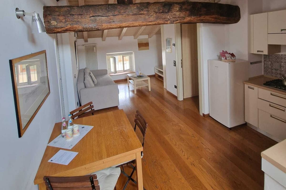 Une pièce spacieuse avec un plafond en bois, une table à manger avec des chaises, un canapé, un coin cuisine équipé d’un réfrigérateur et une fenêtre laissant entrer la lumière naturelle.