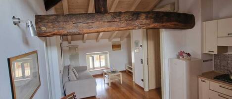 Una habitación espaciosa con techo de madera, una mesa de comedor con sillas, un sofá, una zona de cocina con refrigerador y un ventanal que proporciona luz natural.
