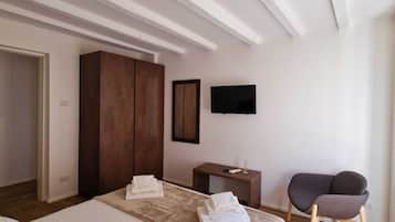 A modern bedroom with a large bed, a wardrobe, a TV, and a seating area.