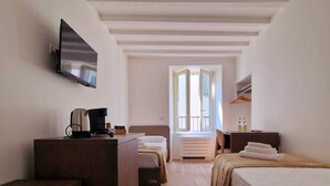 A hotel room with a wooden desk, a bed, a TV mounted on the wall, and a window with a view of the outside. - LocandaMimmo (Bergamo)