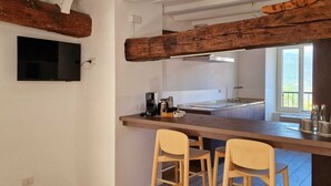 A modern kitchen with a wooden beam ceiling, a flat-screen TV mounted on the wall, and a bar area with stools. - LocandaMimmo (Bergamo)