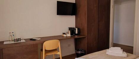 A hotel room with a bed, a desk, a chair, a TV mounted on the wall, and a wardrobe.