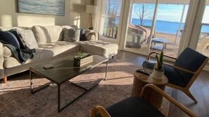 A spacious living room with a large window offering a view of the sea, a white sofa, a coffee table, and a wicker chair.