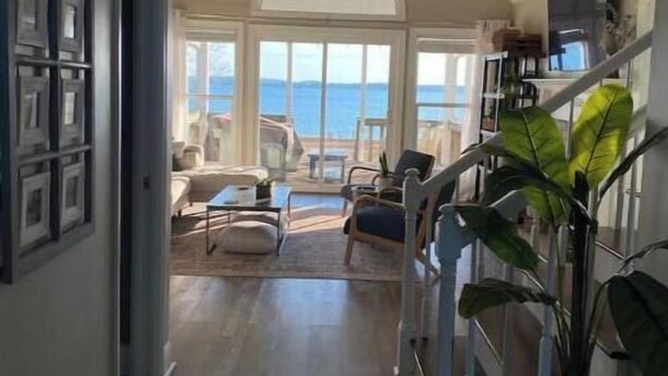 A spacious living area with a view of the sea, a ceiling fan, and a staircase leading to an upper level.