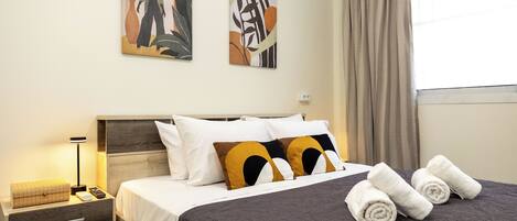 A neatly made bed with a dark patterned bedspread, two pillows with a geometric design, and a bedside table with a lamp and a small decorative item.