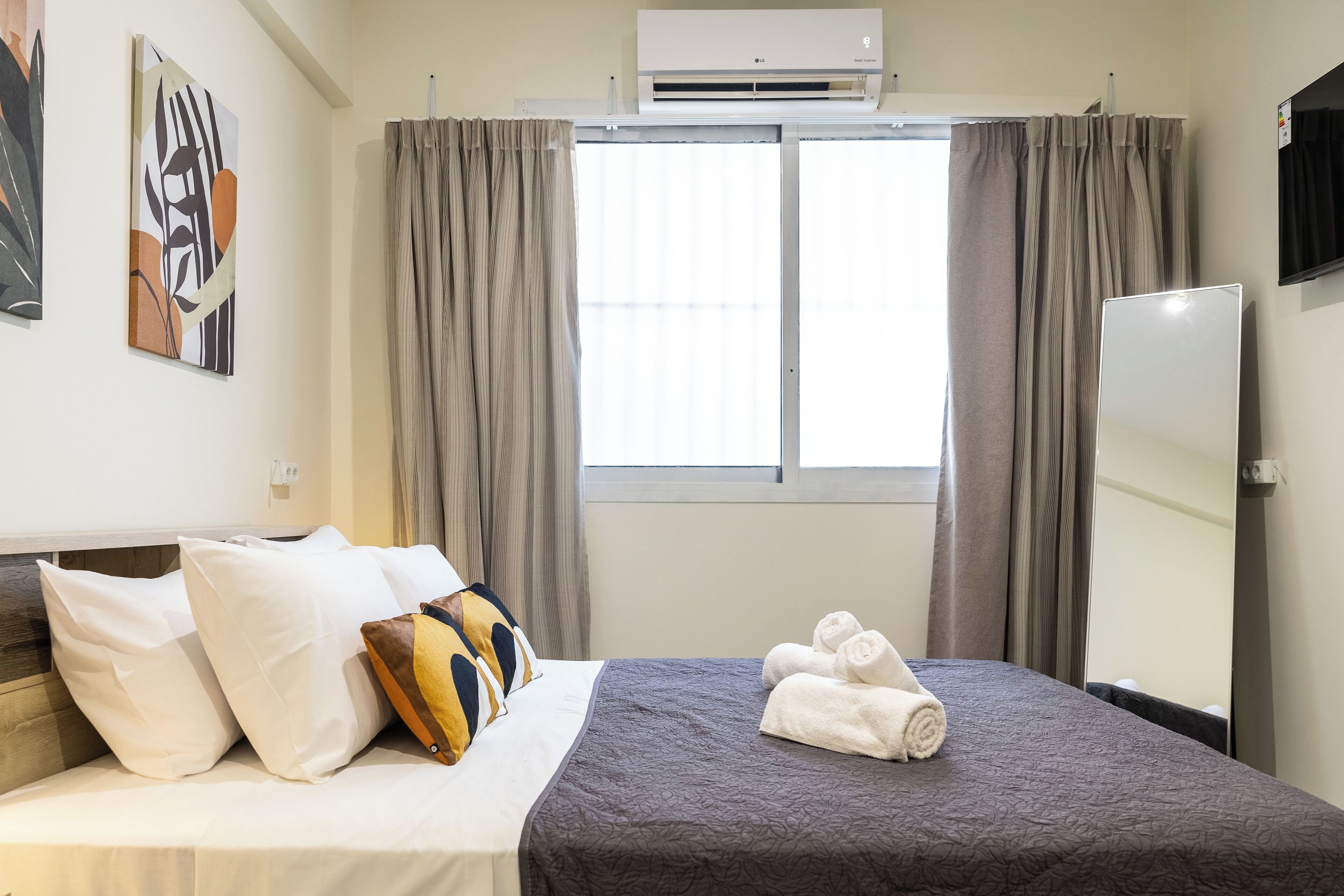 Habitación de hotel con cama, almohadas, manta, ventana con cortinas, aire acondicionado y espejo.