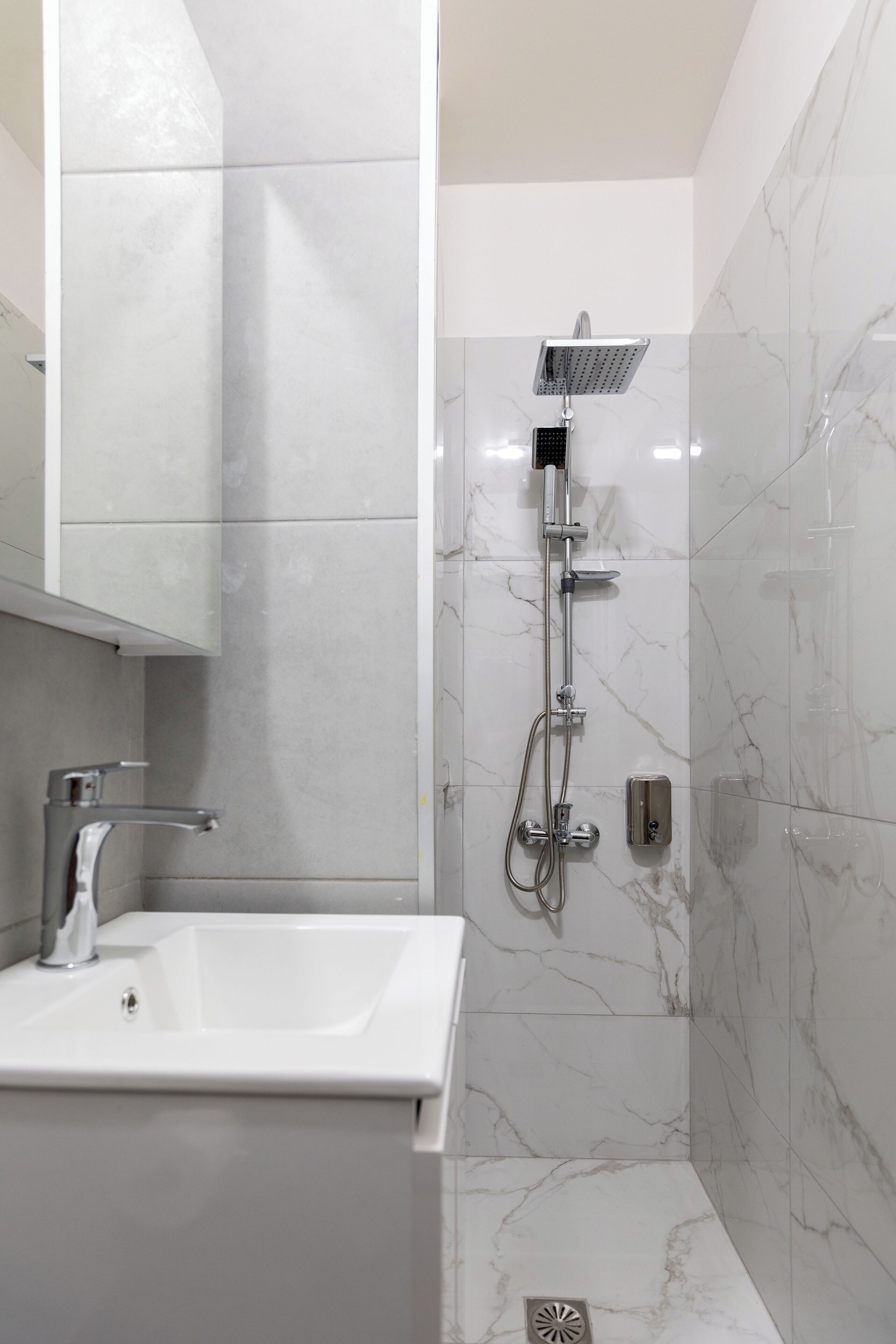 Ein modernes Badezimmer mit einem weißen Waschbecken, einer Handbrause und einem wandmontierten Wasserhahn.
