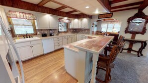 A kitchen with wooden cabinets, a central island, and a dining area with wooden chairs. - Sycamore Cabin with Hot Tub Breathtaking Views (Gaines)