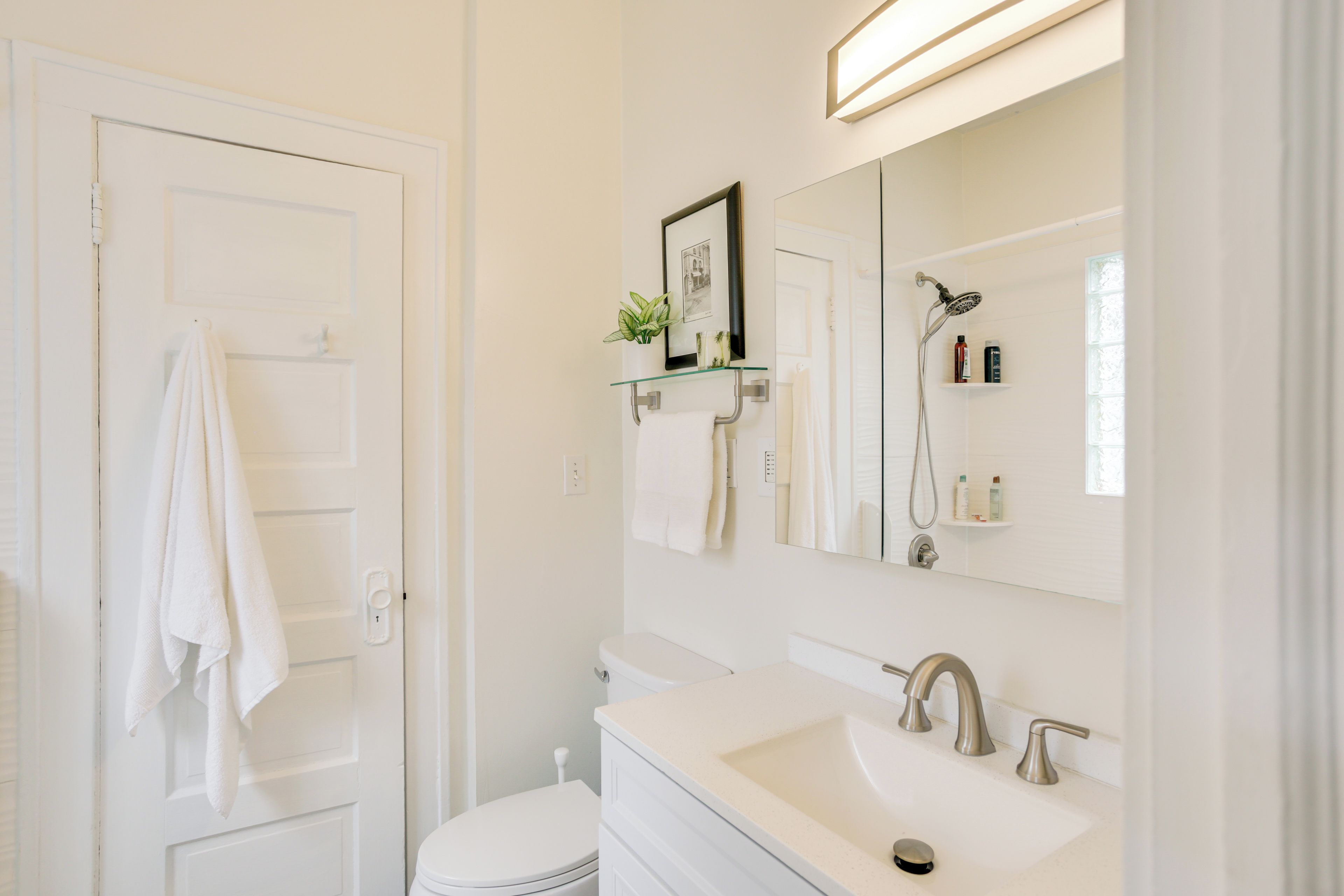 A bathroom with a white toilet, a sink with a mirror above it, and a shower head.