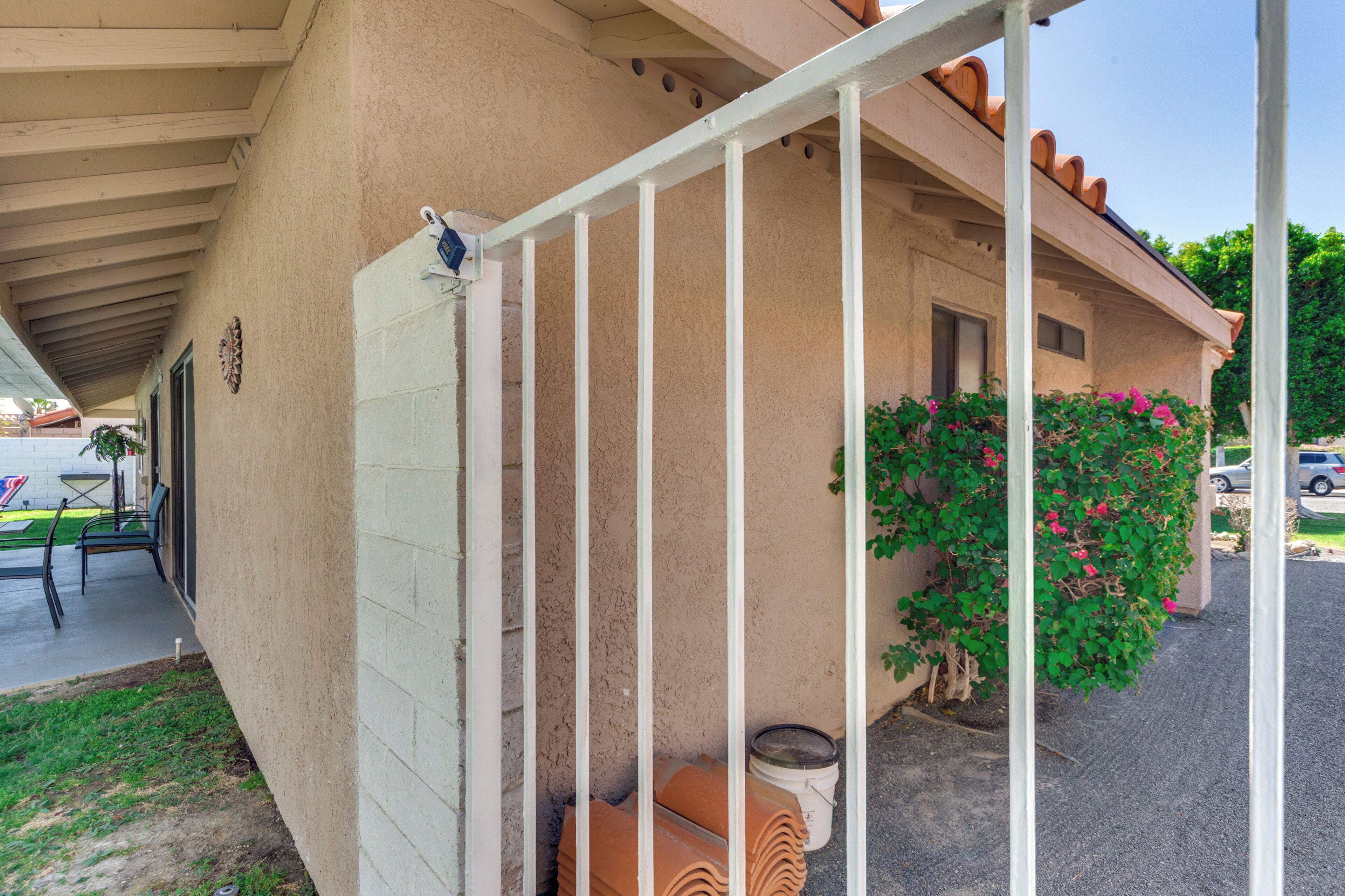 A building with a covered porch, a white railing, and a potted plant with pink flowers.