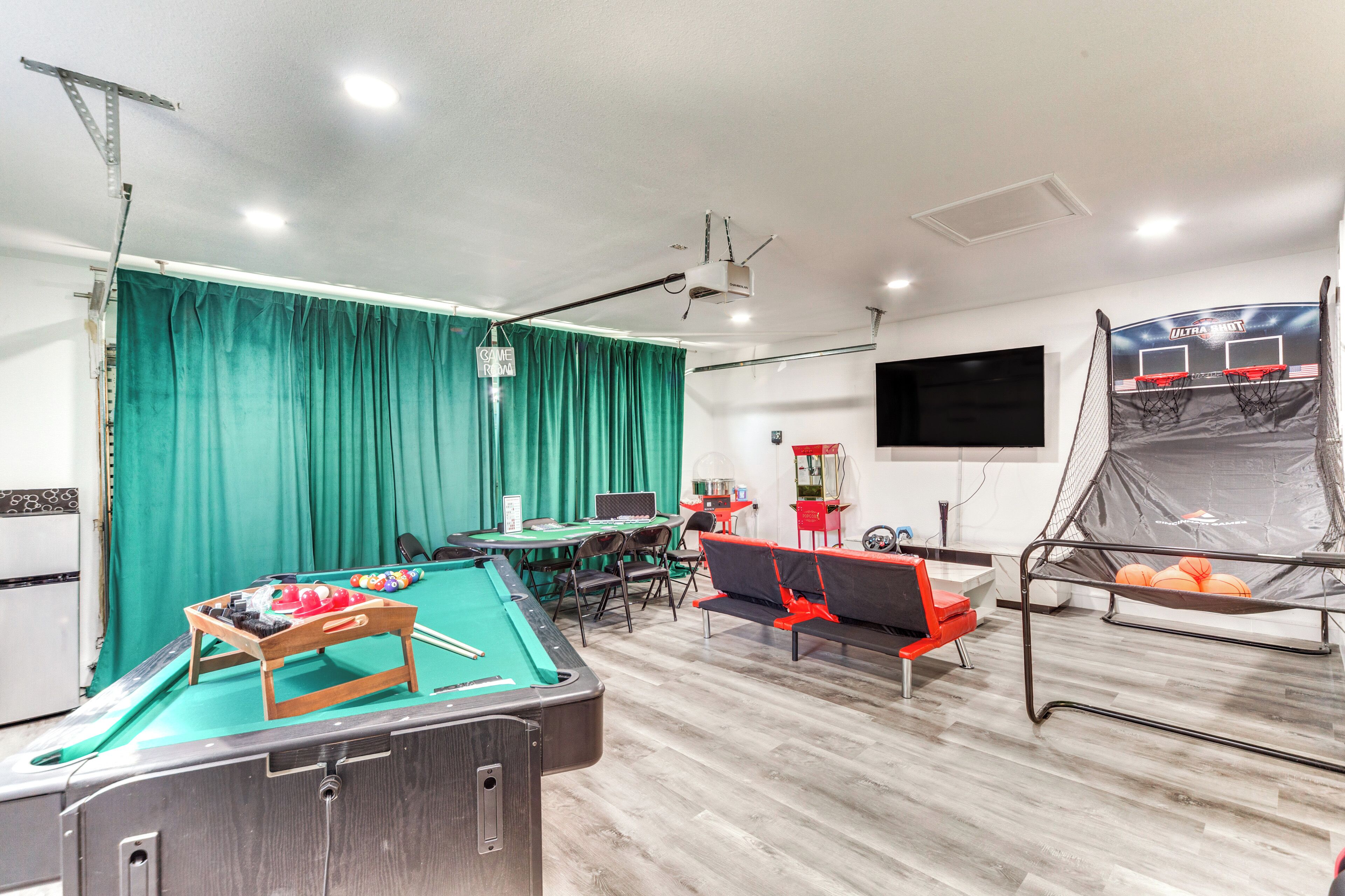 A pool table with a green felt surface, a billiards cue, and a red and black sofa.