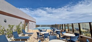 A rooftop terrace with a pool, lounge chairs, and tables. - COARM0104 - Smart Convenções (Salvador)