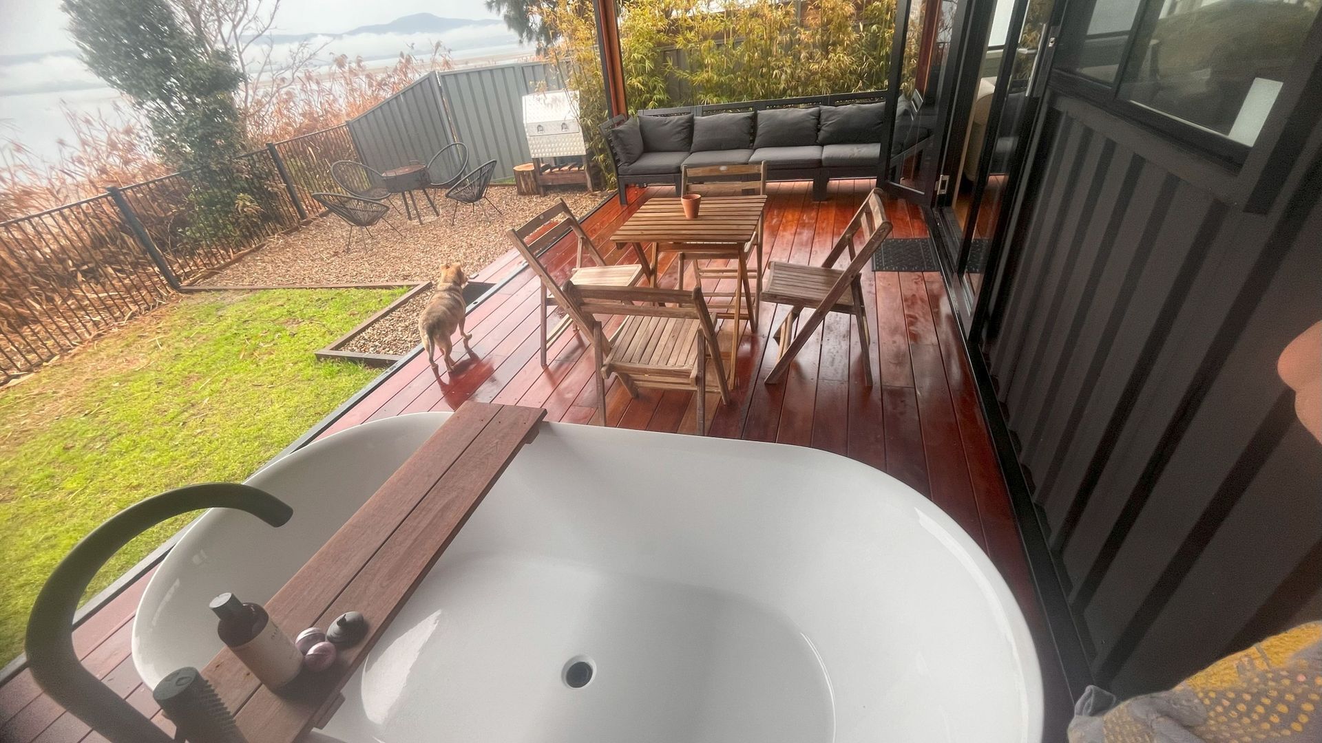 Une terrasse dotée d’une grande baignoire blanche, de meubles en bois et d’un canapé.