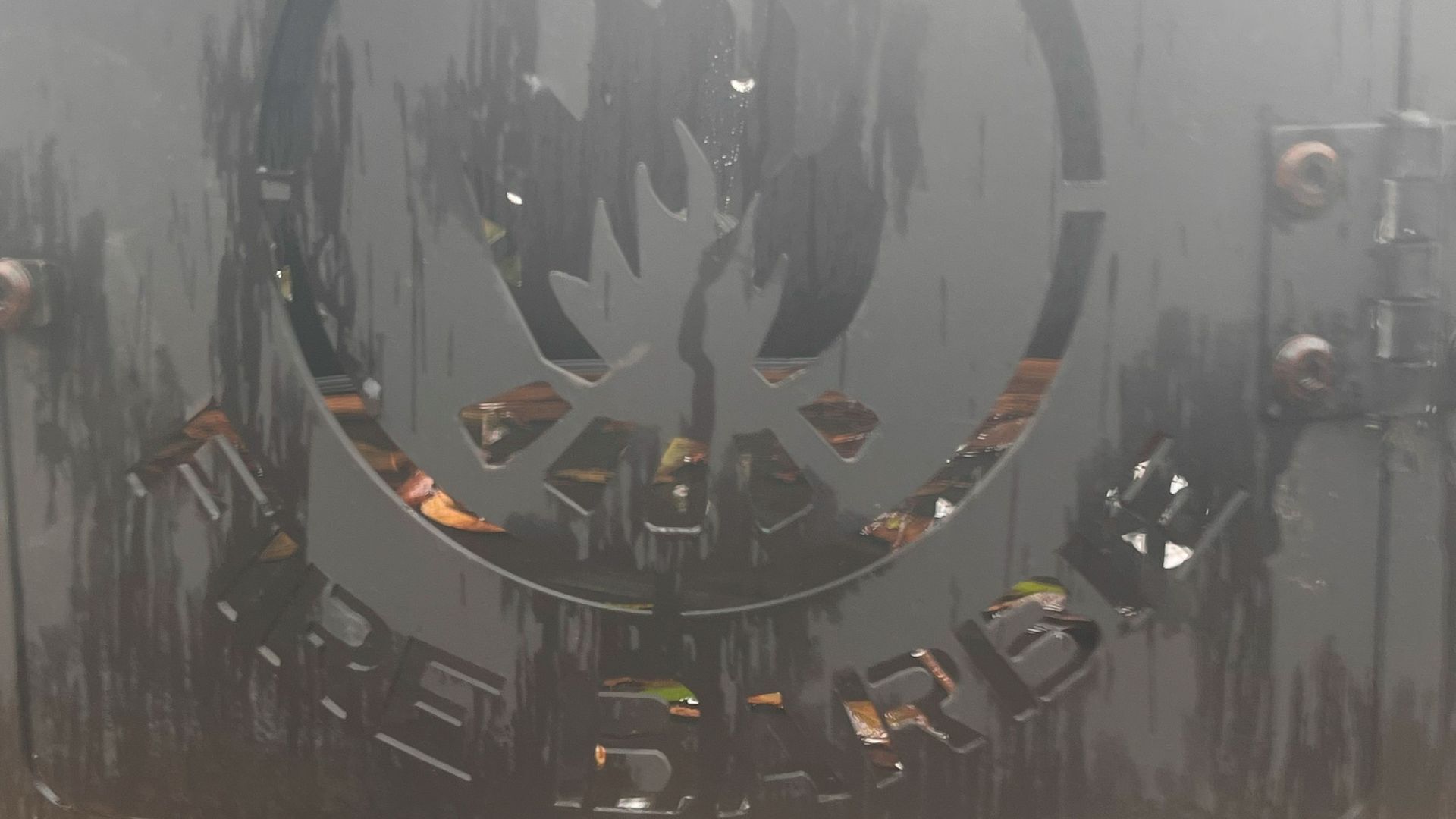 Un emblème circulaire orné d’un motif central, entouré d’un cadre métallique fixé par des rivets.
