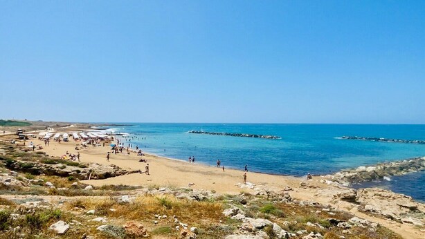 A beach with rocky terrain, clear blue water, and a few people. - Venus Beach | Elegant 1BR Apt | 100m From Sea | Groundfloor (Paphos)