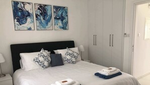 A neatly made bed with white and blue linens, a dark headboard, and decorative pillows. There are two folded towels on the bed. - Venus Beach | Elegant 1BR Apt | 100m From Sea | Groundfloor (Paphos)