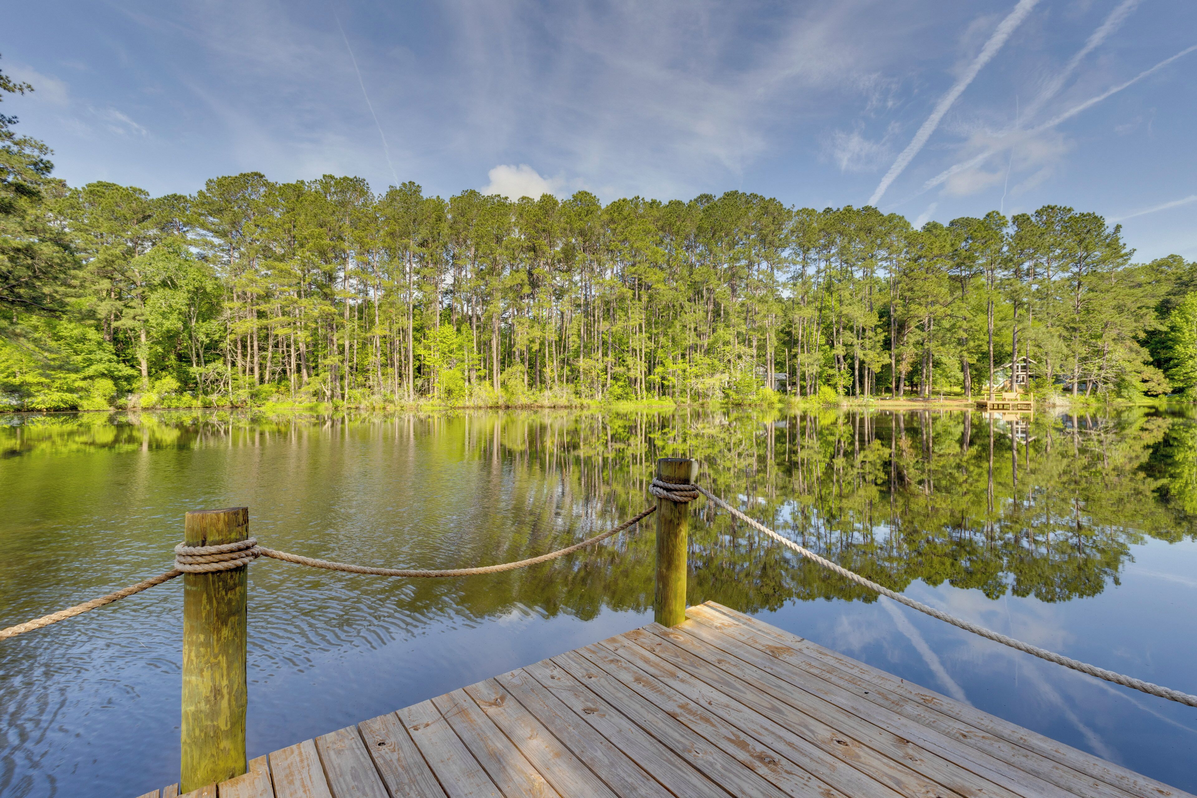 A wooden dock extending into a calm lake, surrounded by dense forest and clear skies.