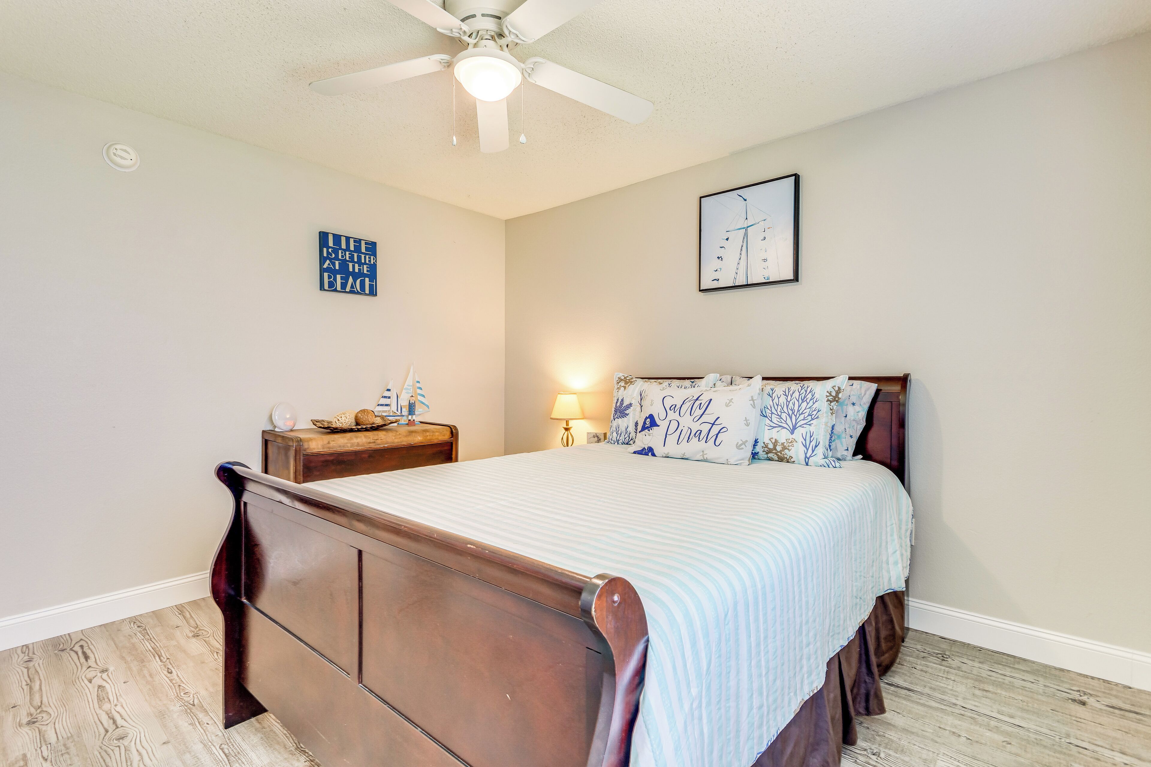 A bedroom with a wooden bed, a nightstand, a ceiling fan, and a wall clock.