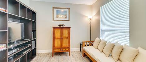 Una sala de estar con un mueble de madera, un sofá con cojines, un televisor y un cuadro en la pared.