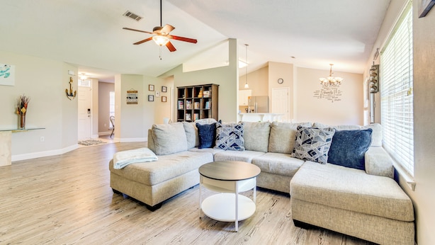 A spacious living room with a sectional sofa, a round coffee table, and a ceiling fan. - 6 Mi to Navarre Beach: Dog-friendly Home w/ Yard (Navarre)