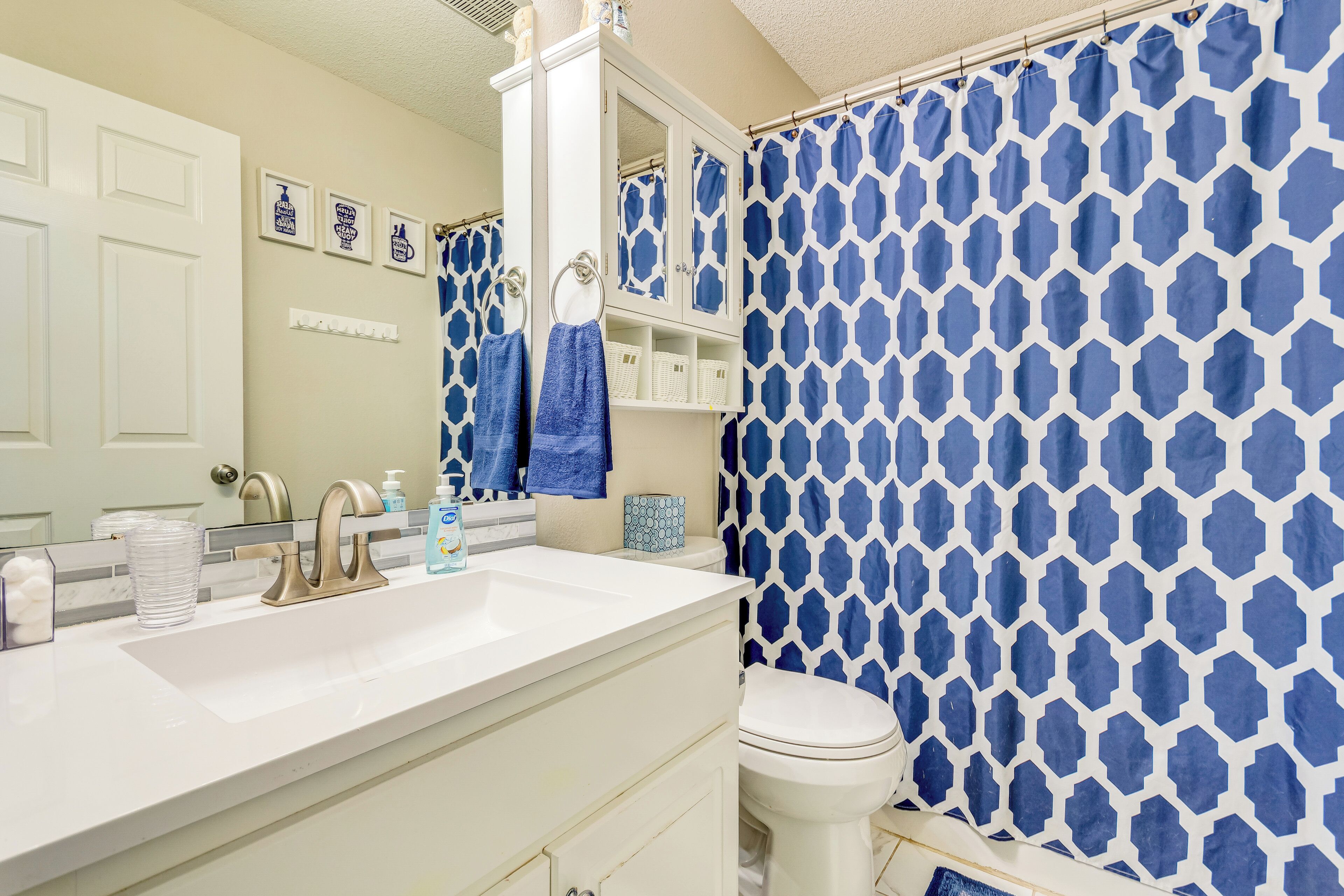 A bathroom with a white sink, a mirror, a toilet, and a blue shower curtain.