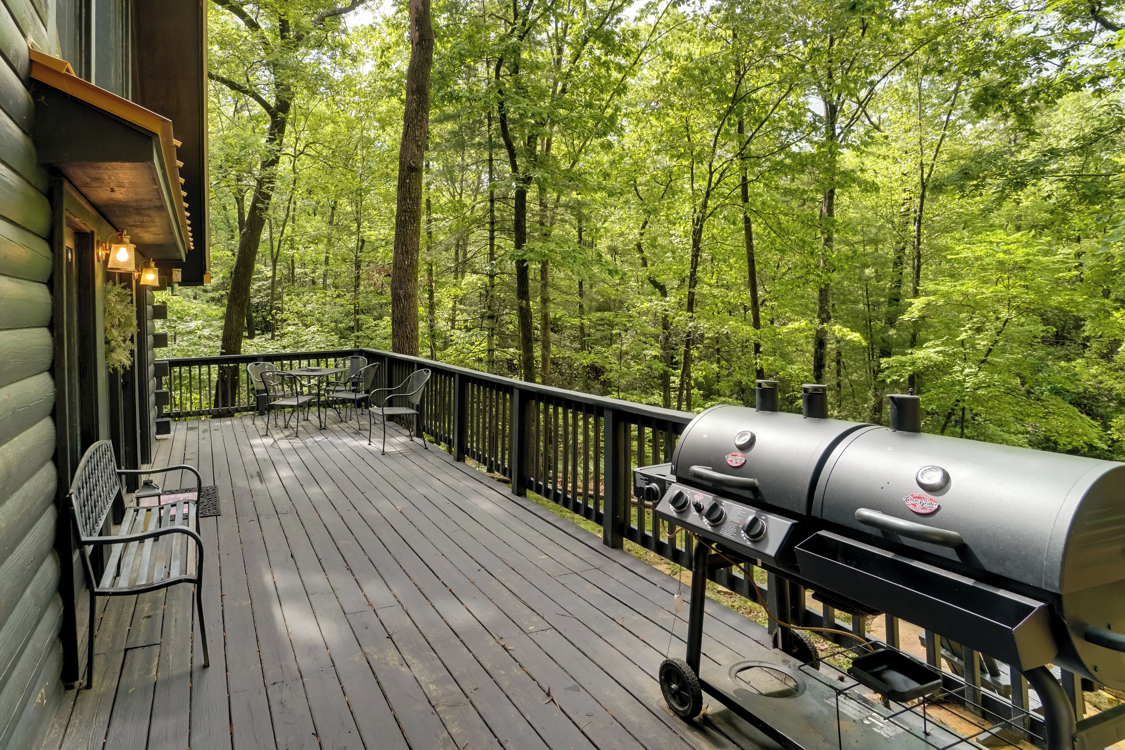 A wooden deck with a grill and benches, surrounded by a forest.