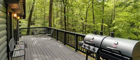 A wooden deck with a grill and benches, surrounded by a forest.
