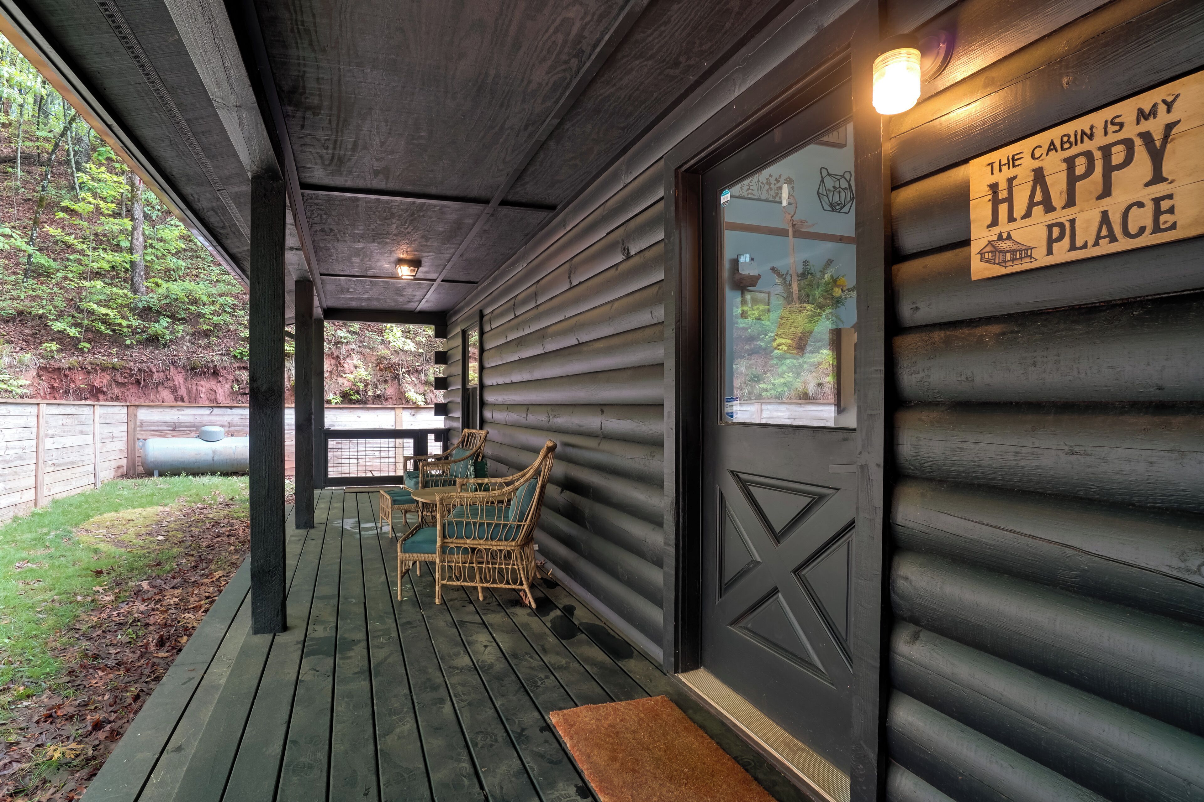 A wooden cabin with a porch, a sign reading "The cabin is my happy place," and wicker chairs.