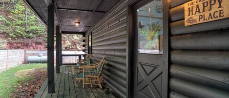 A wooden cabin with a porch, a sign reading "The cabin is my happy place," and wicker chairs.