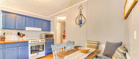 Una cocina compacta con armarios azules, una encimera de madera y una zona de comedor con mantel a rayas y sillas azules.