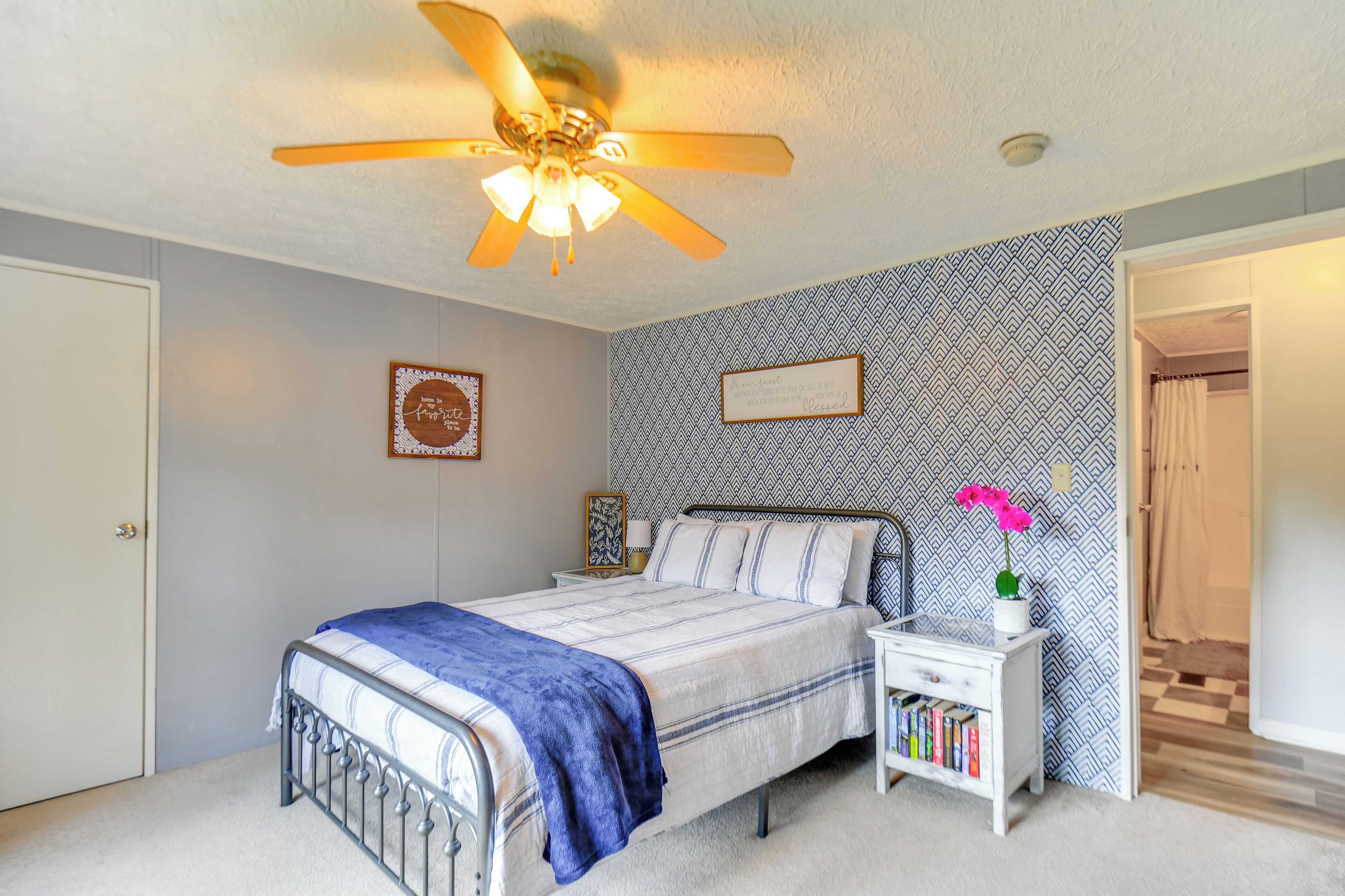 A bedroom with a bed, a nightstand, a ceiling fan, a patterned wall, and a door.
