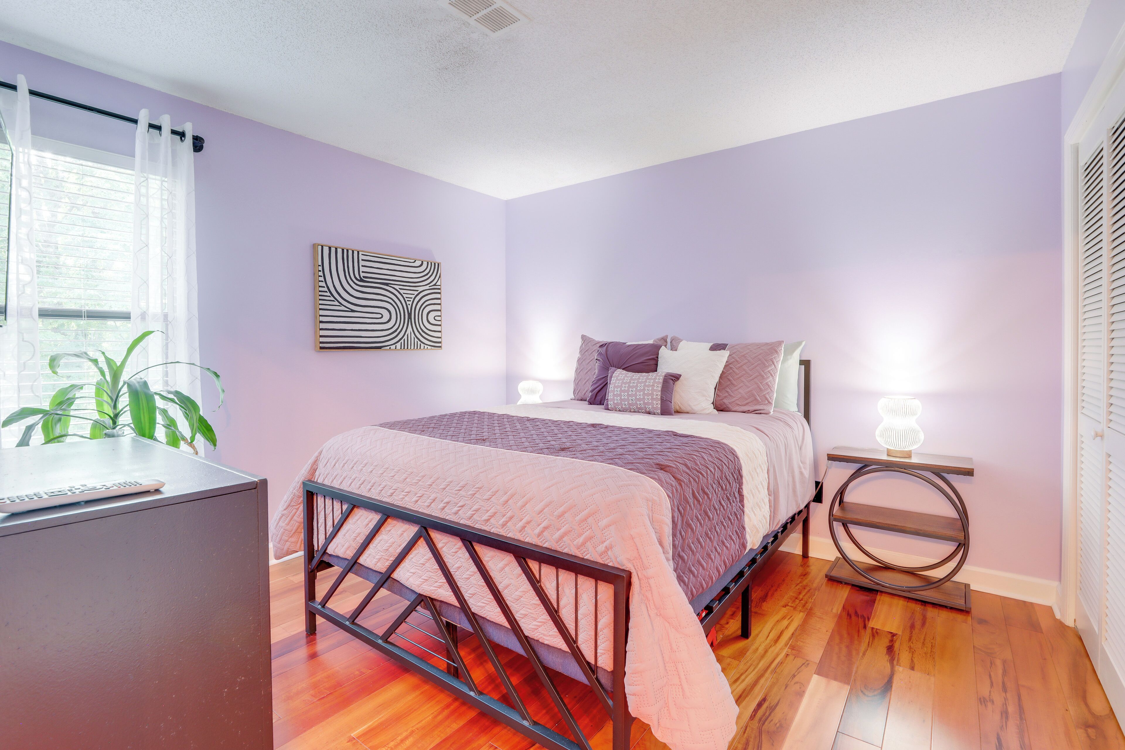 Une chambre à coucher avec un lit, un bureau, une plante et une œuvre d’art murale.