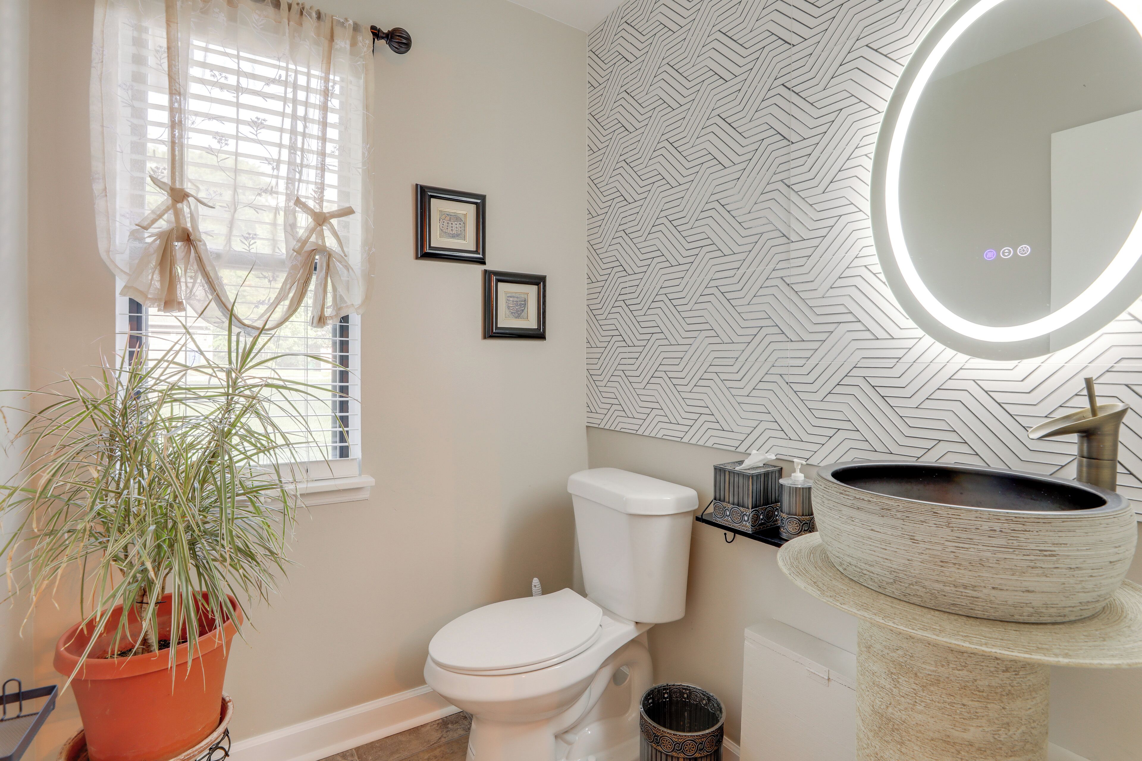 A bathroom with a toilet, a sink with a mirror, a potted plant, and a patterned wall.